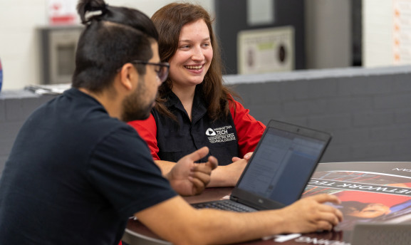 Two student in the commons around a table working at a laptop