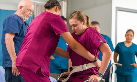 CNA student assisting another individual to get out of a wheelchair