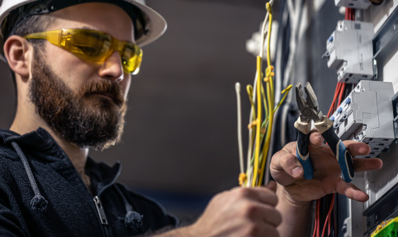 An electrician working on an electronic switchboard with pliers