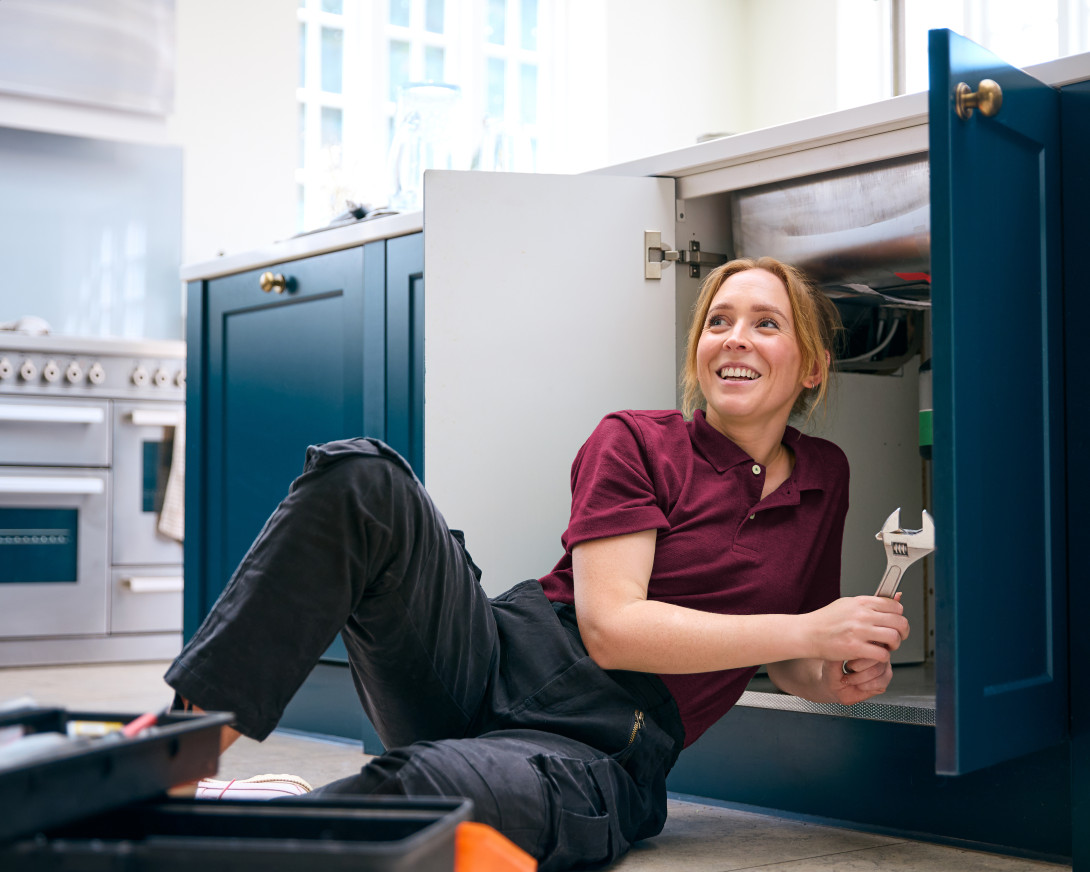 Female plumber fixing waste disposal under kitchen sink